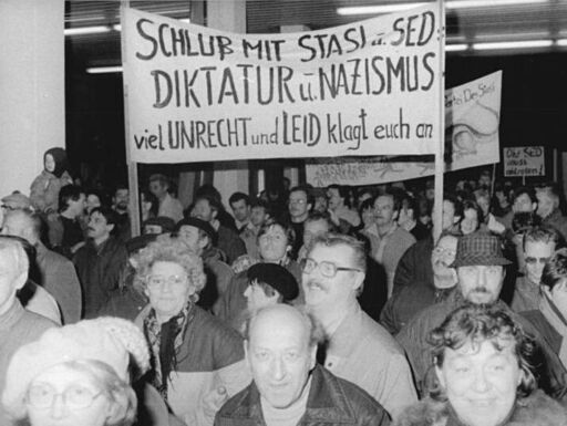 Demonstrierende mit großem Transparent mit dem Text "Schluss mit Stasi u. SED-Diktatur u. Nazismus. Viel Unrecht und Leid klagt euch an"